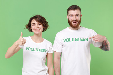 Smiling two friends couple in white volunteer t-shirt isolated on green background. Voluntary free...