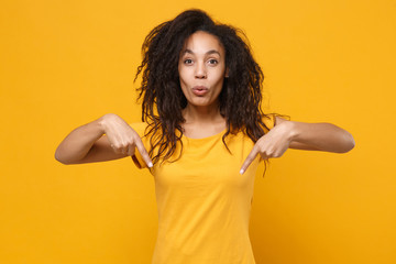 Amazed young african american woman girl in casual t-shirt posing isolated on yellow orange wall...