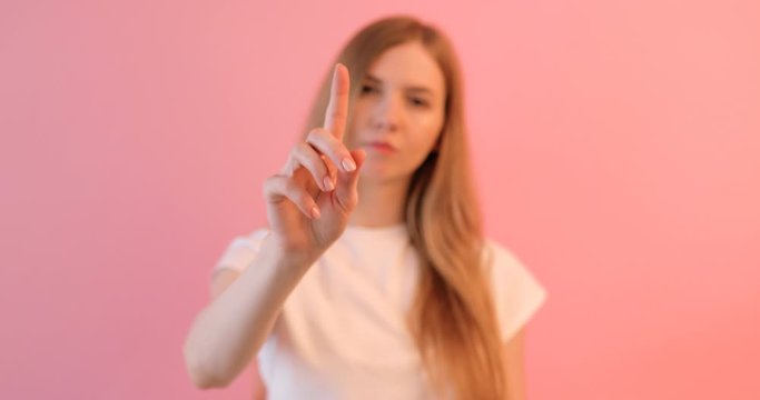 A woman in a white t-shirt touches an imaginary screen with her finger,on a pink background, points with her finger