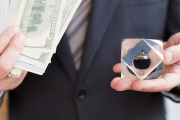 Businessman in suit, tie holds in hands drop of black oil of Brent brand in crystal cube.Pack of...