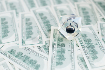 Drop of black oil of Brent brand in crystal cube laying on the background of hundred dollars bills....