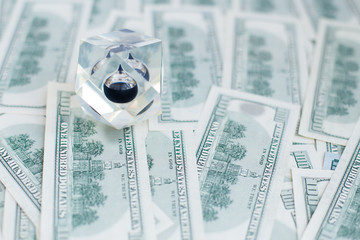 Drop of black oil of Brent brand in crystal cube laying on the background of hundred dollars bills....