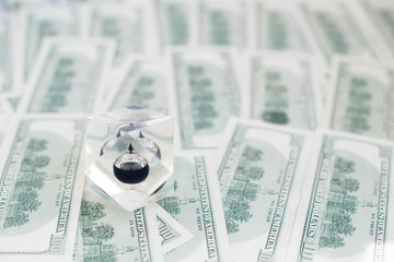 Drop of black oil of Brent brand in crystal cube laying on the background of hundred dollars bills....