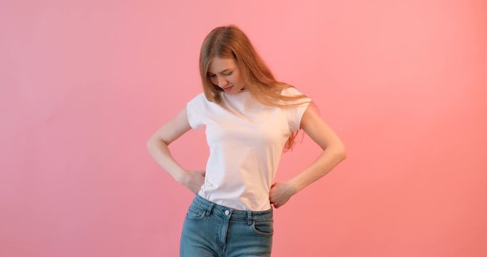 Portrait of a happy girl in a white t-shirt showing arm muscles on a pink background