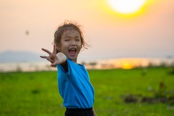 Asian girl kindergarten children wear blue shirts, standing, playing at the water's edge when the sun is about to set.