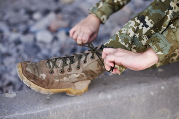 Close-up picture of military khaki green ankle boots. Two woman's hands tying shoelaces on army...