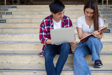 Asian male and female students sit and review the textbook, discuss the study in your free time do...