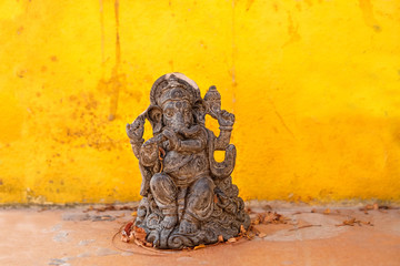 Old statue of God Ganesha on yellow wall background. Ganesha Hindu Idol symbol of success, wisdom, prosperity. copy space