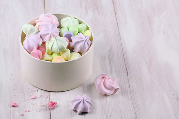 Colored Meringue Cookies in a white box, on a light wooden background.
