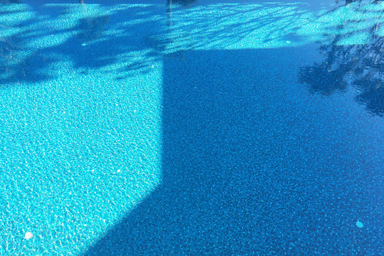 Shadow reflection image of building and trees on the bottom of freshness and crystal clear swimming pool with wavy surface of water in summer season.