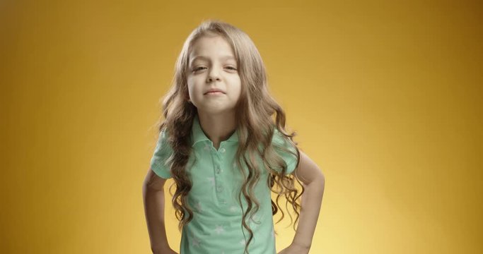 Little caucasian girl looking at camera in misunderstanding, then getting surprised and happily dancing, isolated on yellow background - emotions concept close up 4k