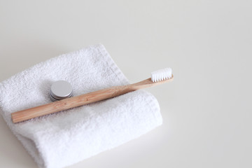 Bamboo toothbrush laying on a table with towel and aluminium container for toothpaste 