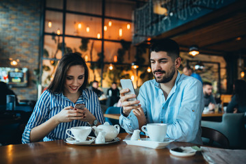man and woman couple using mobile devices in cafeteria