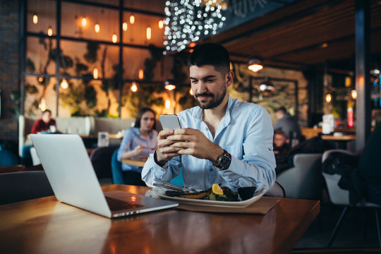 man using mobile phone and laptop in restaurant while having lunch