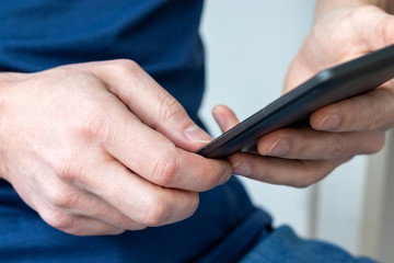 Gray e-reader electronic book in male hands. A man in a blue t-shirt with a tablet. Selective focus