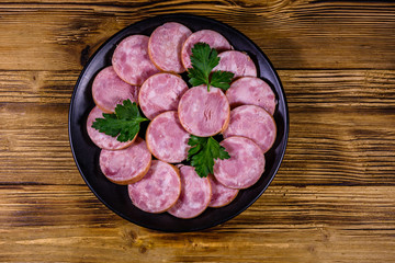 Black plate with sliced sausage on a wooden table. Top view
