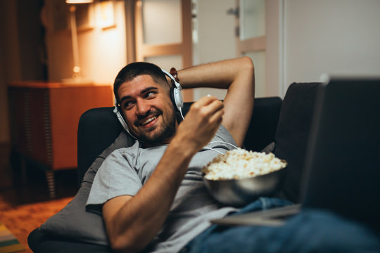 Young Man Laying Sofa And Eating Popcorn At His Home