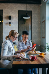 women friends eating in restaurant, using mobile phone