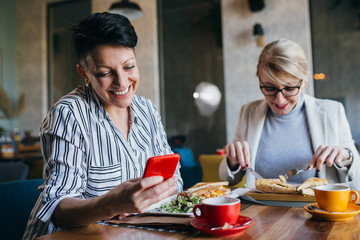 mid aged women using mobile phone while having lunch break with her friend