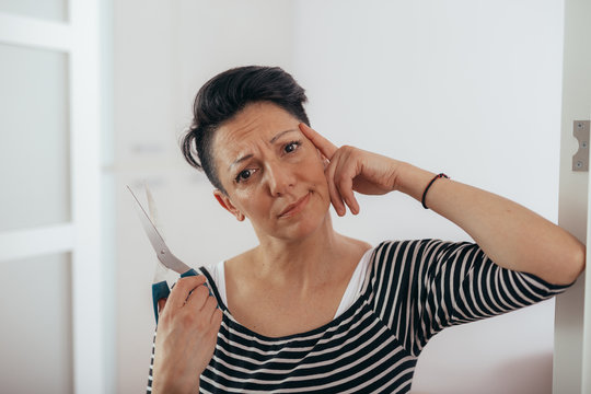doubt and thoughtful mid aged woman holding scissors for cutting her hair