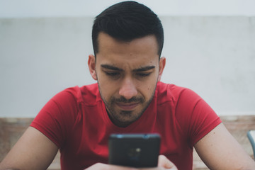 retrato de un chico joven y guapo,sentado mirando su smartphone