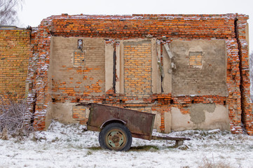Destroyed brick building with a rusty trailer, view from the front.