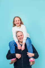 Brother giving piggyback ride to smiling sister on blue background. Father holds laughing happy...