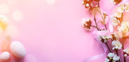 Art Easter banner with painted eggs and spring flowers on light pink background. Top view, flat lay with copy space.