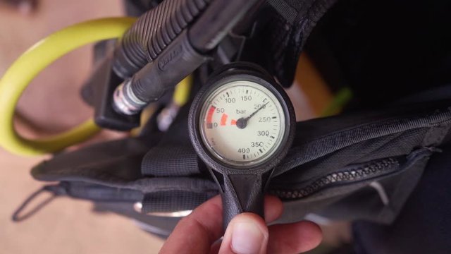 Before a scuba dive someone checks their air to be sure the tank has enough air. pressure gauge shows two hundred bars of pressure.