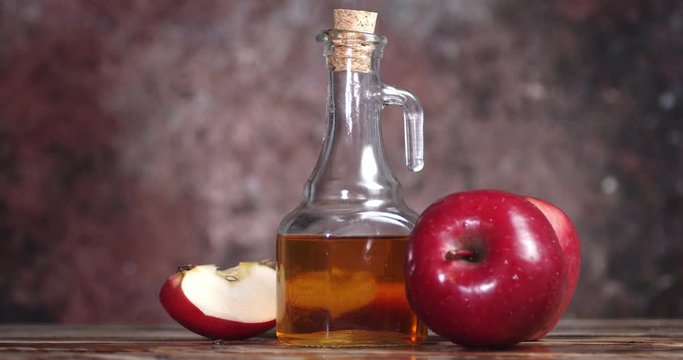 Apple cider vinegar is rotating on a wooden table.