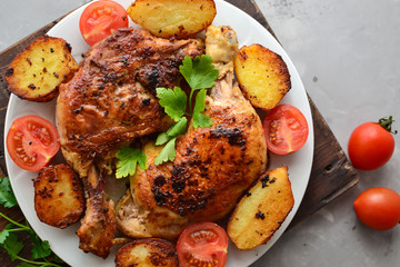 Fried chicken thigh, baked chicken leg. Top view. Dark background. Plate on a wooden board. Baked potatoes, tomatoes and chicken, a delicious lunch.