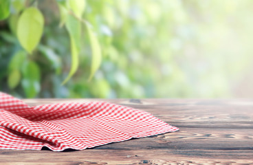 Red checkered picnic cloth on wooden table natural blurred background,product display.