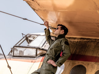 A handsome young pilot standing on the wing of a plane