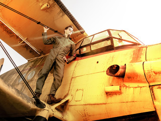 A handsome young pilot standing on the wing of a plane