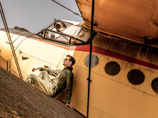 A handsome young pilot sitting on the wing of a plane