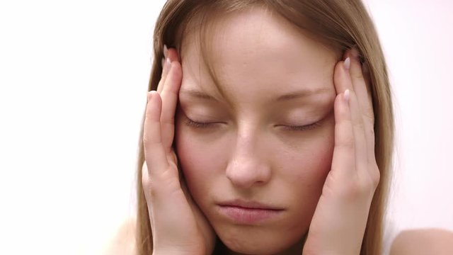 A blonde woman looks dizzy holding her temples with both hands - closeup shot