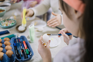 Cropped girl painting white egg with brush