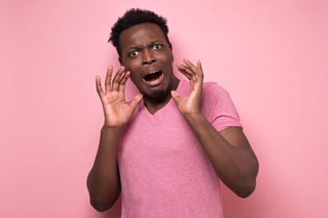 Funny african american scared man in pink shirt with worried expression. Studio shot on colored...