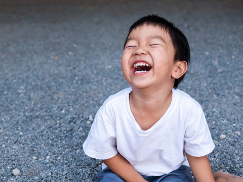 Naklejki Asian cute little child boy laughing with mouth open wide, seeing whitening teeth. Happy Kid in white shirt enjoy in funny shot in relaxing day.