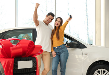 Happy couple with car key in modern auto dealership