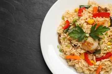 Delicious rice pilaf with chicken and vegetables on black table, closeup. Space for text