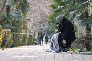 An elderly homeless woman sits in the street. Poverty. Cold. Aging.