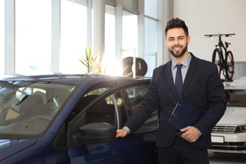 Young salesman with clipboard near car in dealership