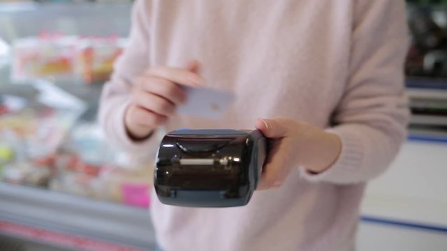 The woman enters data into the payment terminal and applies a Bank card to it. Hands close-up. Shop Windows in the background. Concept of purchases with a Bank card