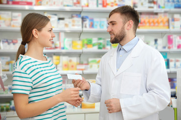 Professional pharmacist giving pills to customer in modern drugstore