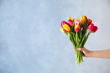 Woman holding beautiful spring tulips on light blue background, closeup. Space for text