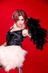 Beautiful retro woman from the roaring 20s is posing on the chair on red background