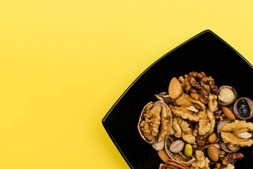 Flat lay ketogenic diet. A mix of walnut,pistachios,pecan,almond in the black square plate on the yellow background. Concept of healthy food.Copy space for mock up