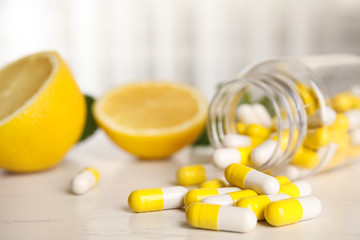 Bottle with vitamin pills and lemon on light table, closeup