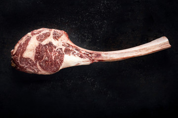 Raw Tomahawk steak dry aged with on a dark stone background, top view and copy space